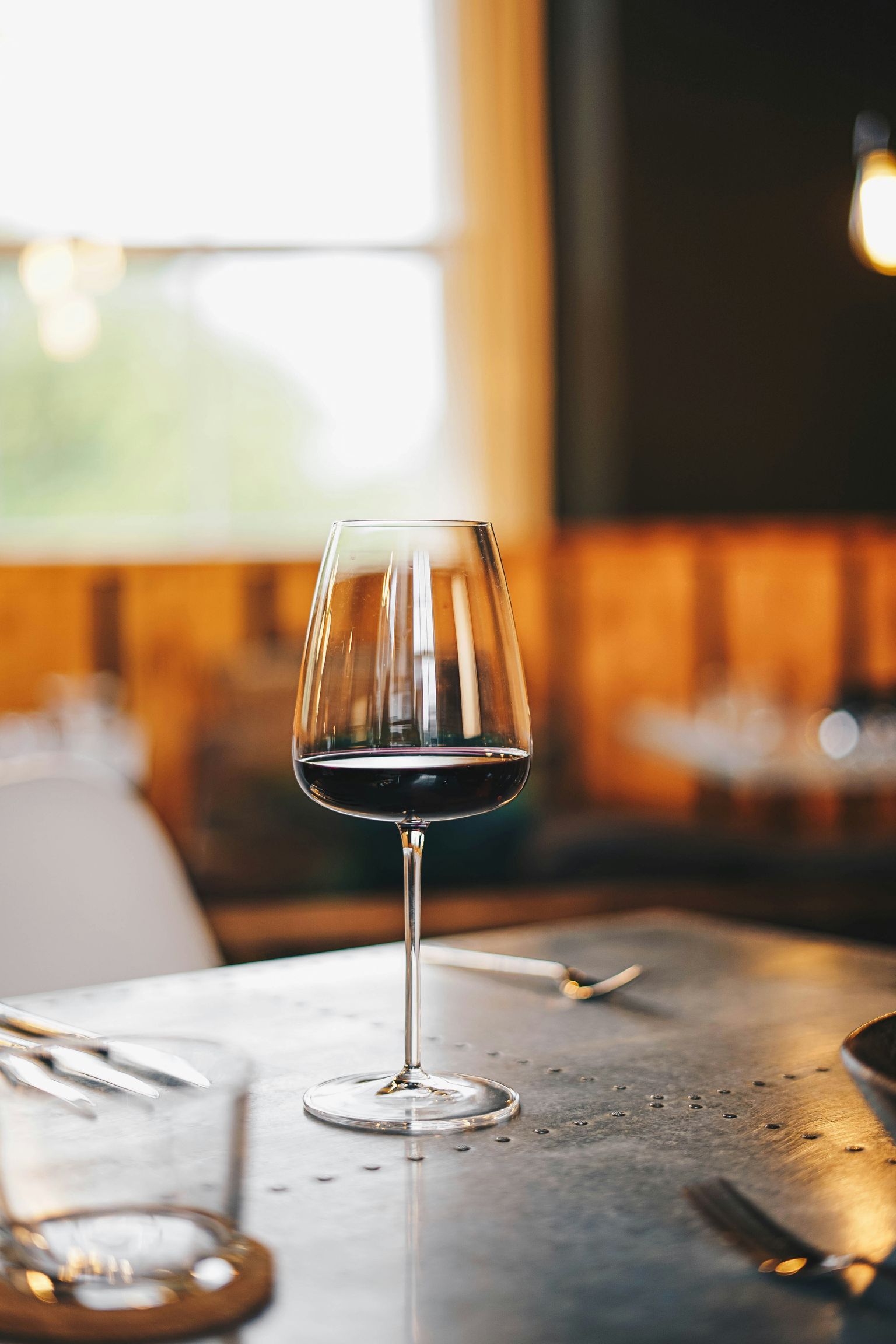 Elegantes Weinglas mit Rotwein auf rustikalem Tisch in gemütlichem Restaurant.