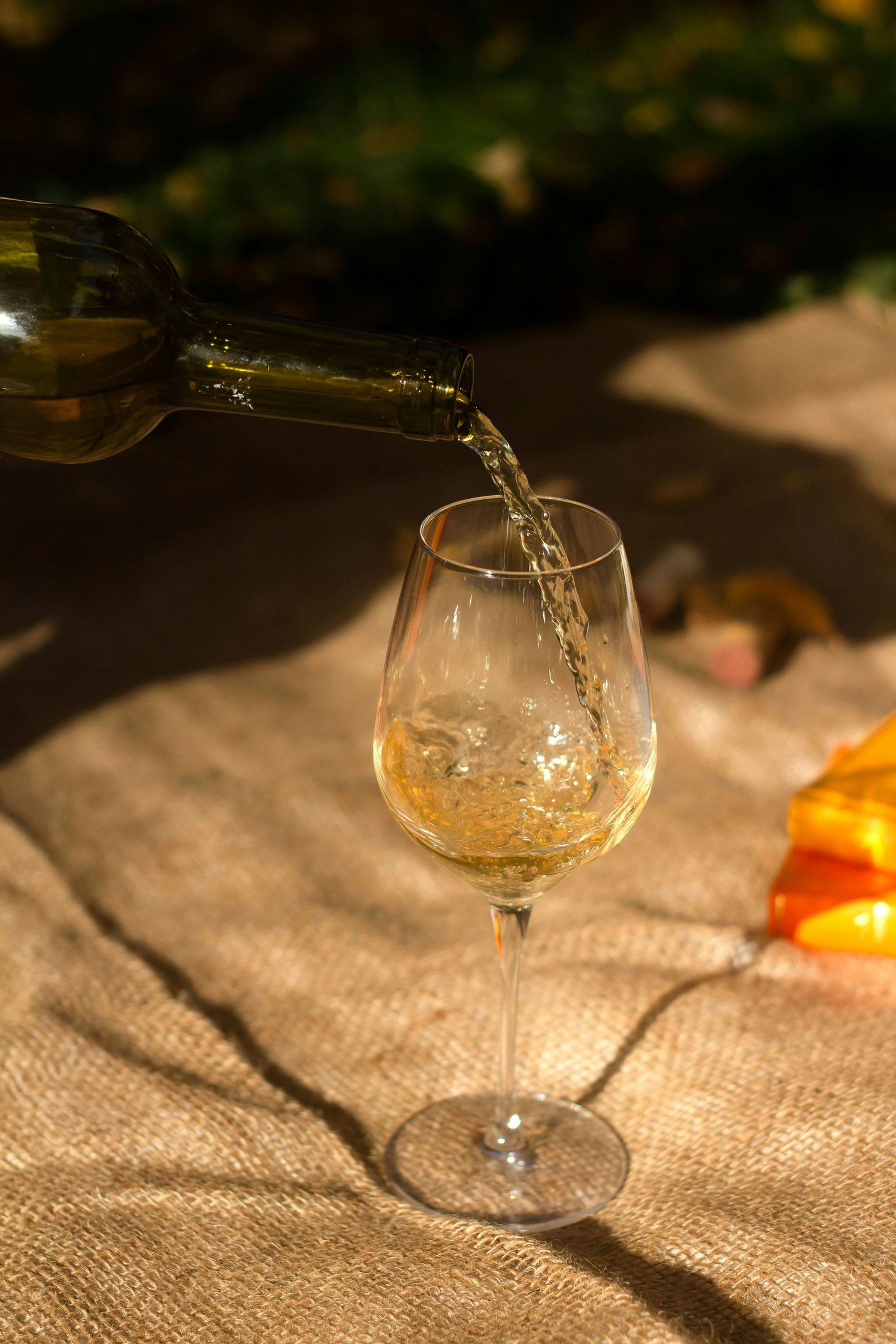 Wein wird aus Flasche in ein Glas auf buntem Tuch gegossen, sonniges Ambiente.