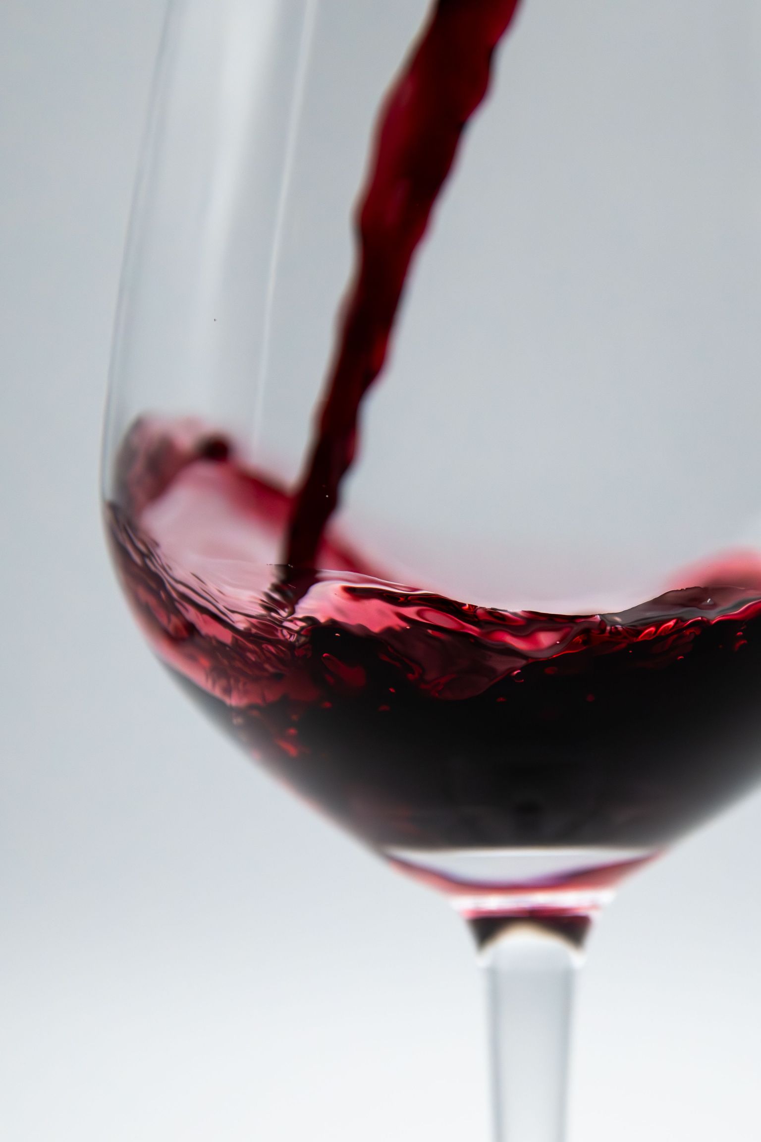 Rotwein fließt elegant in ein gefülltes Weinglas.