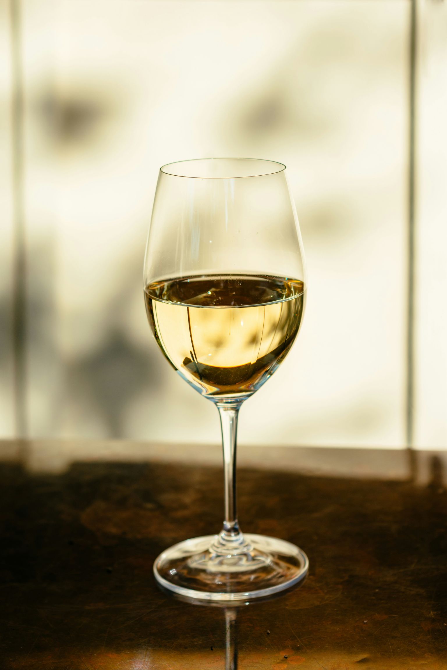 Ein Glas helles Wein mit klarem, goldgelbem Inhalt auf dunklem Tisch.