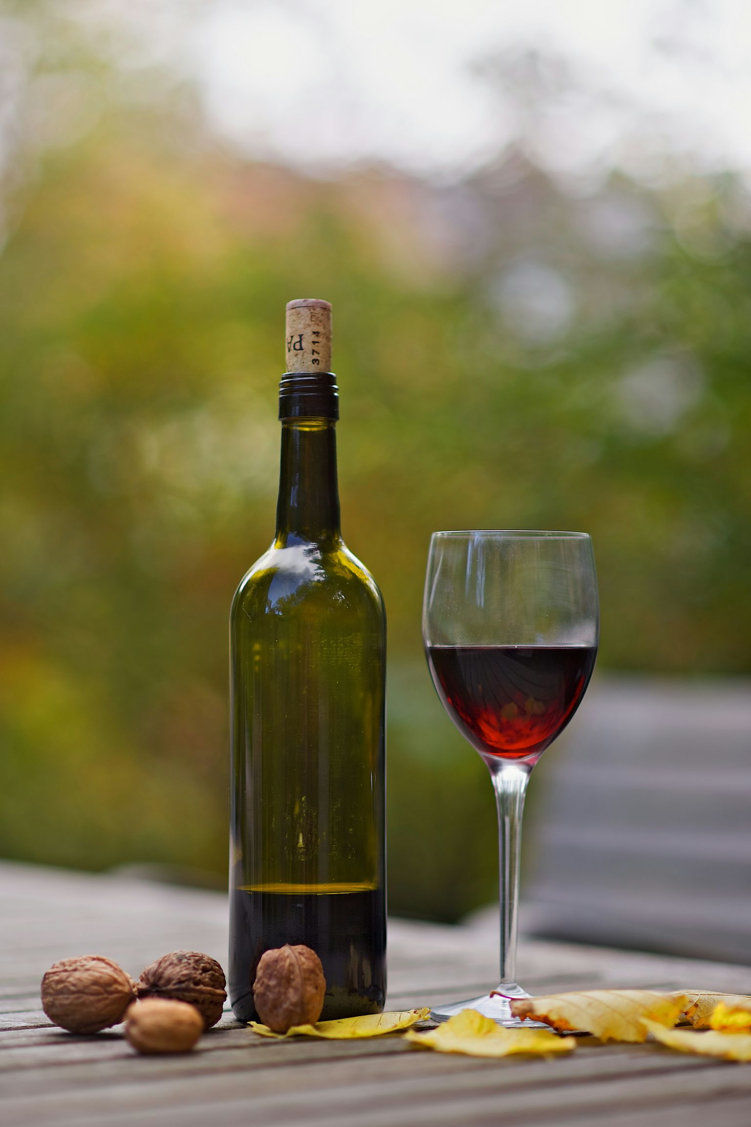 Glass Wein mit Flasche und Nüssen auf Holztisch im Freien.