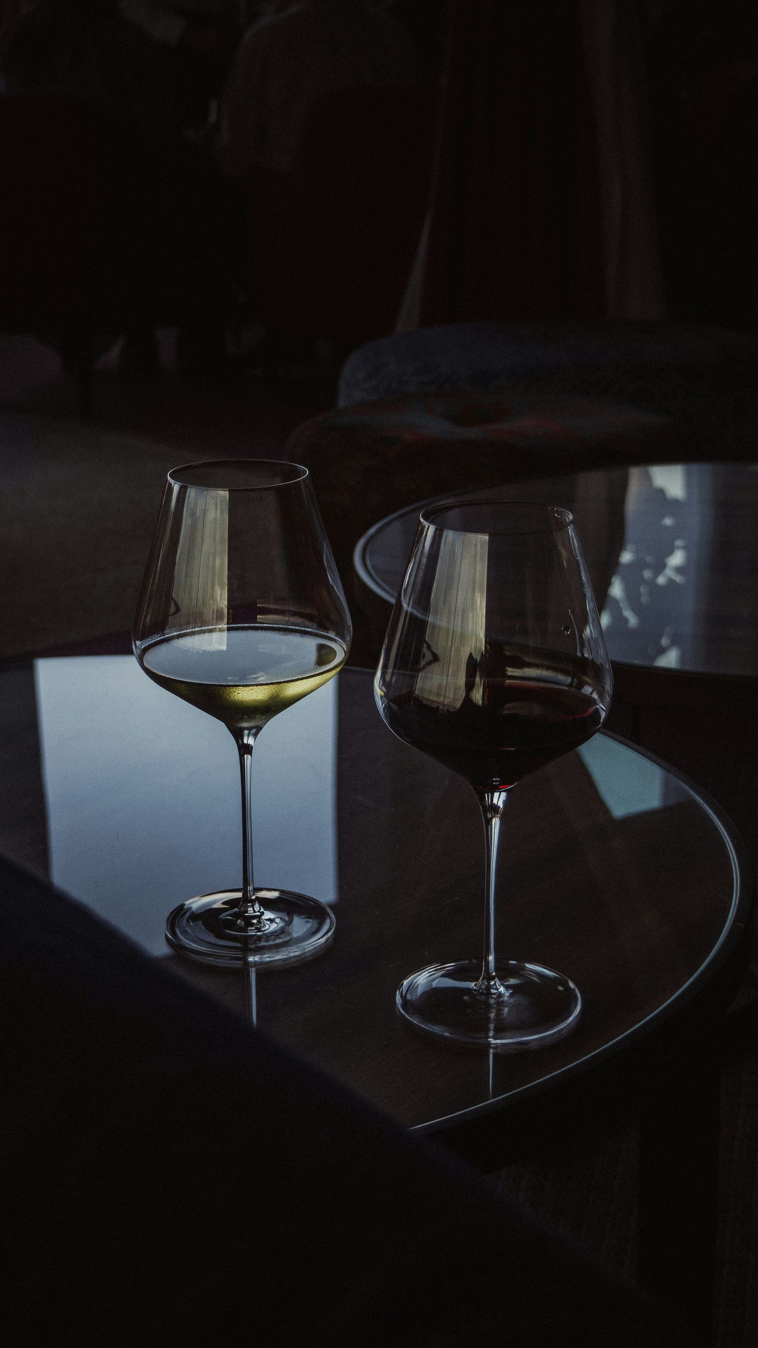 Zwei Weingläser mit hellem und dunklem Wein bei gedimmtem Licht.